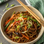 Close-up of a vibrant bowl of homemade Chinese Chow Mein noodles with colorful vegetables and green onions, ready to eat.