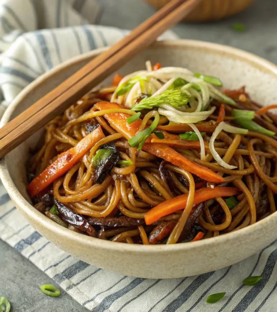 Close-up of a bowl of vegetarian Chow Mein noodles with carrots, mushrooms, and green onions, garnished with fresh sprouts and chopsticks