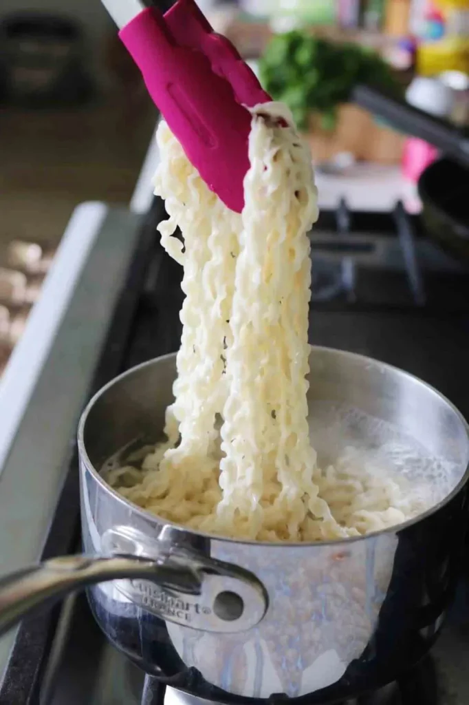 Fresh hand-pulled noodles lifted from boiling water using pink silicone tongs