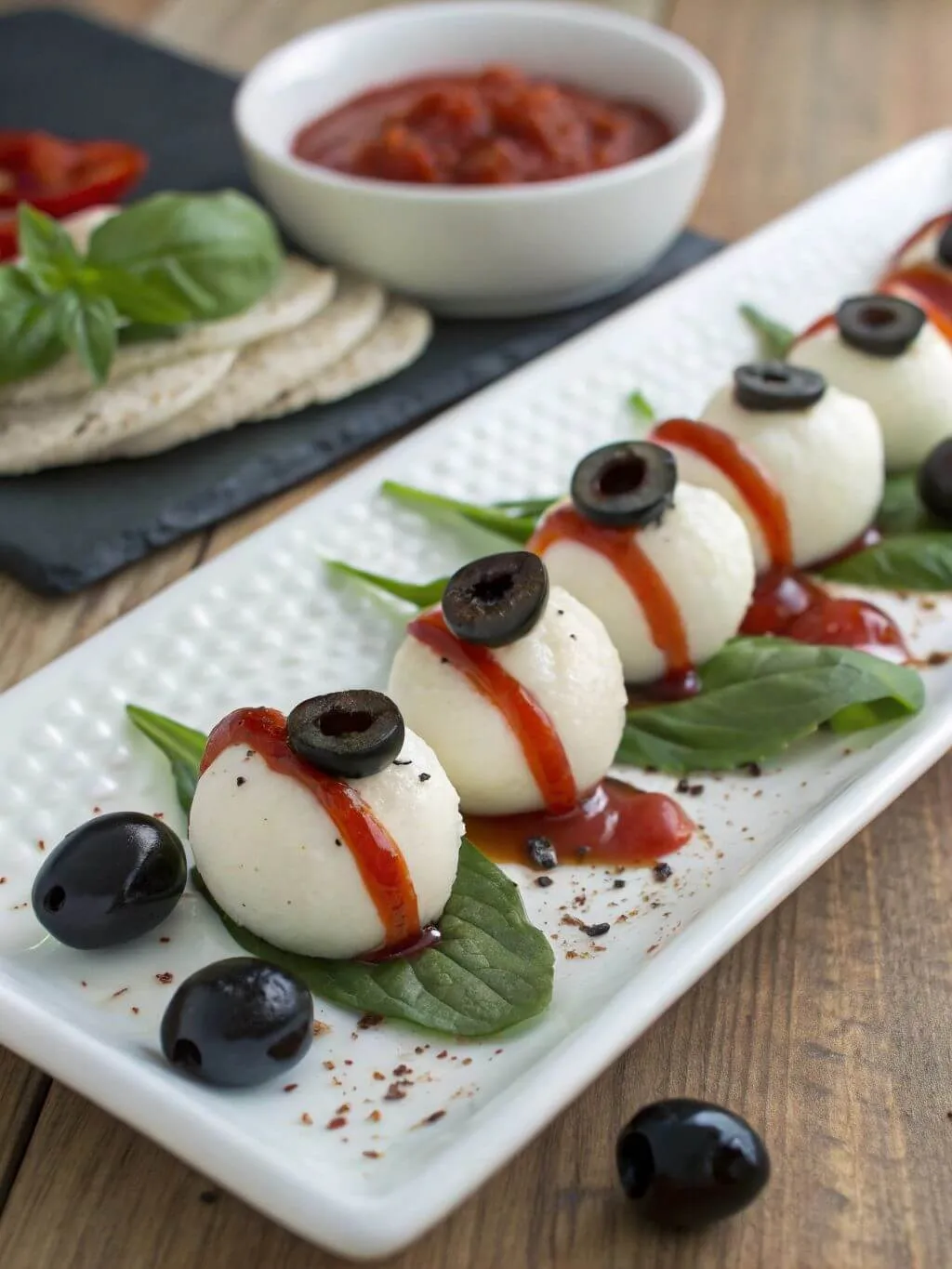 Create the Mozzarella “Eyeballs” Halloween mozzarella eyeball appetizer with black olives and red sauce