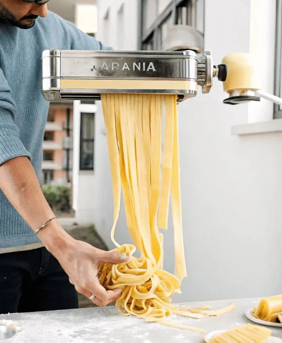 Cut Person rolling fresh pasta dough through a pasta machine outdoors