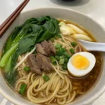 Bowl of hand-pulled noodles in rich broth with beef, bok choy, and soft-boiled egg