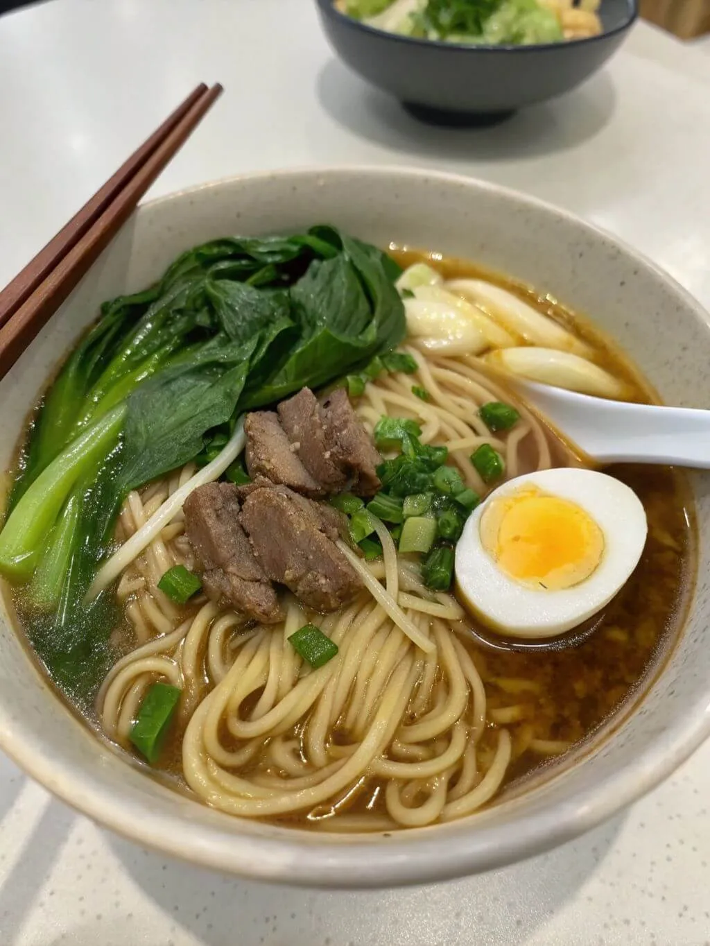 Bowl of hand-pulled noodles in rich broth with beef, bok choy, and soft-boiled egg