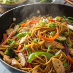 Lo Mein noodles with chicken and mixed vegetables in a large black wok, ready to be served, with steam rising.