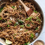 Sesame soba noodles tossed in sauce with scallions and sesame seeds in a pan