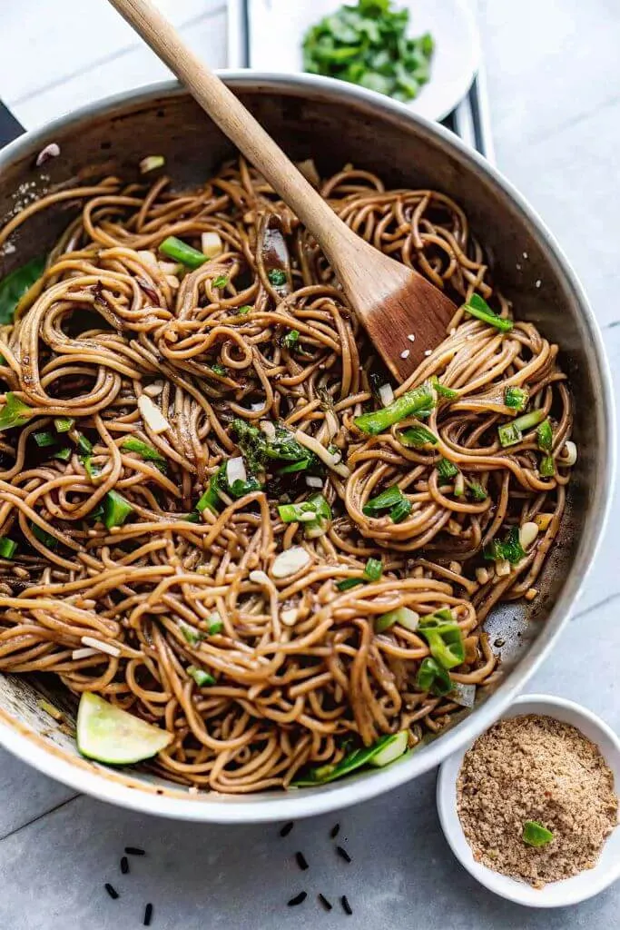 Sesame soba noodles tossed in sauce with scallions and sesame seeds in a pan