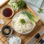 Chilled somen noodles served with dipping sauce, cucumber, green onions, seaweed, sesame, and ice on a bamboo tray