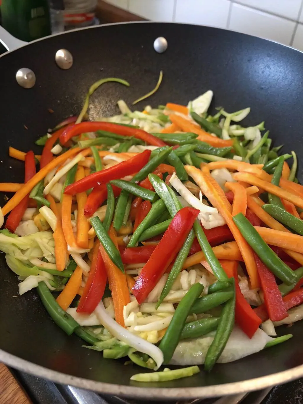 A close-up shot of a wok filled with colorful, chopped vegetables including red bell peppers, carrots, and green beans, being stir-fried.