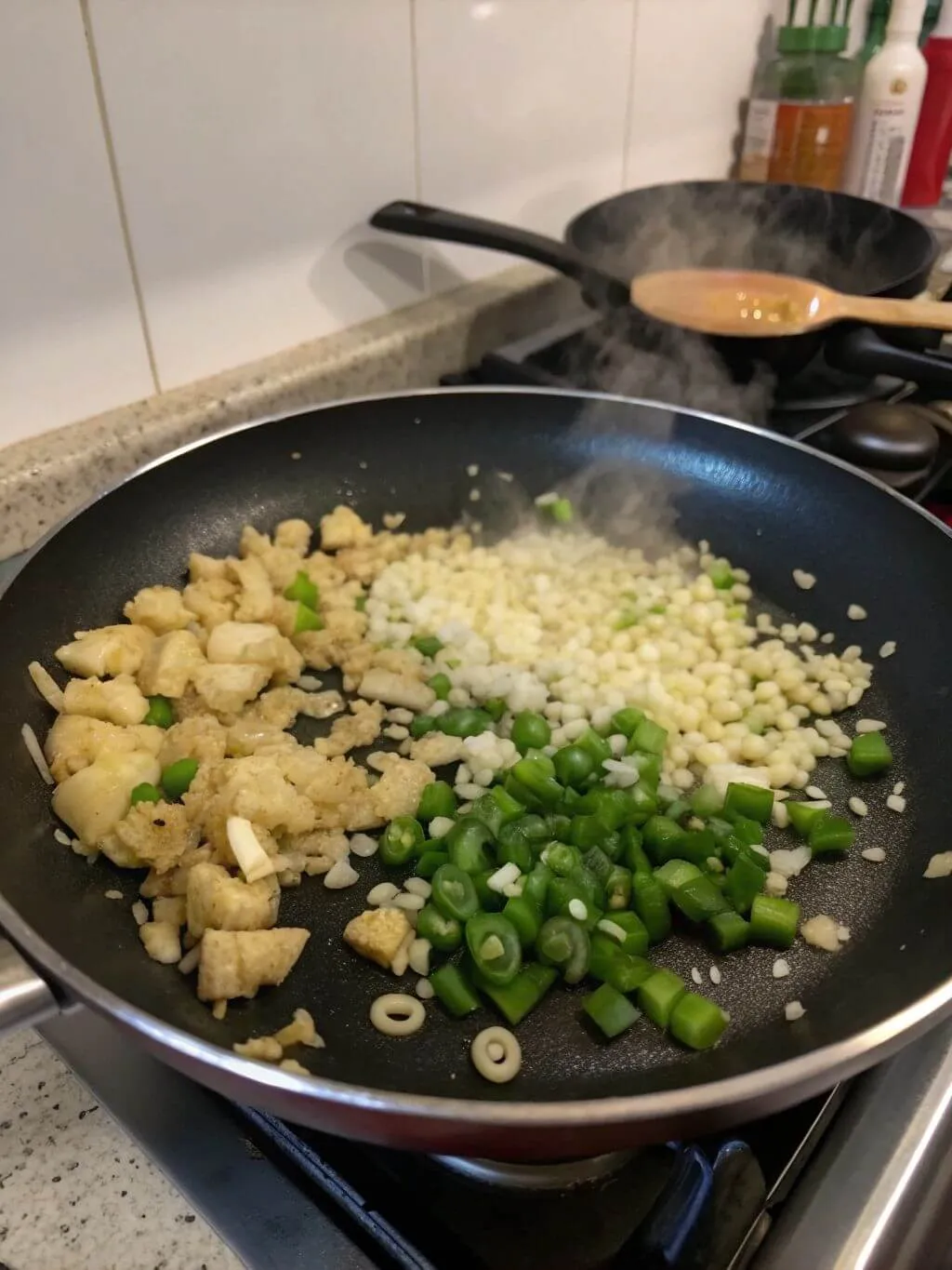 A pan on a stovetop with minced garlic, chopped green chilies, and what appears to be tofu or chicken pieces being stir-fried.